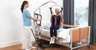 A carer using a mobile hoist to transfer a care home resident from a bed to a chair